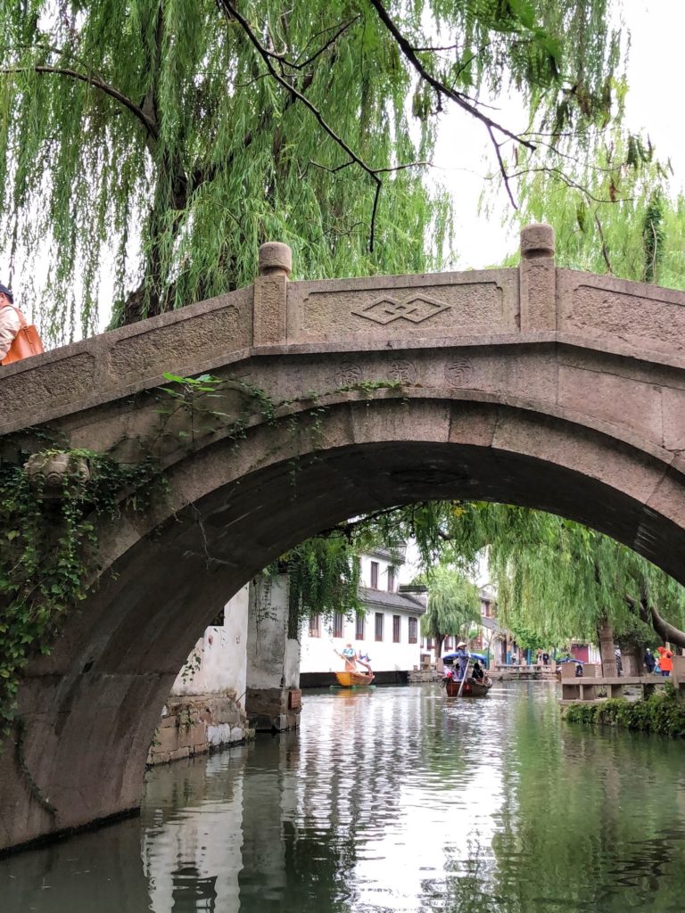 Picture of an ancient stone bridge crossing over the river with hanging trees in the background.