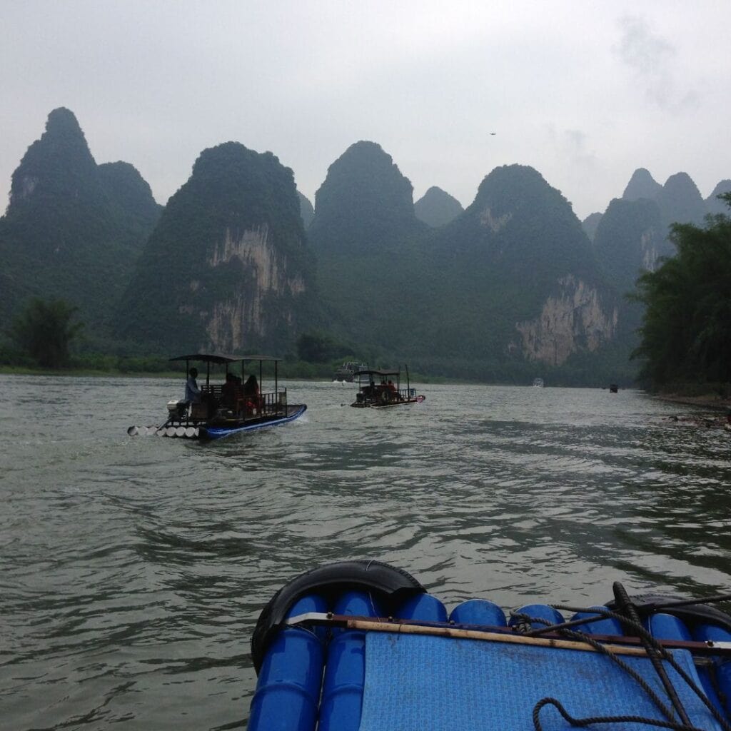 A blue raft boat floating down the Li River toward a rounded karst mountain.