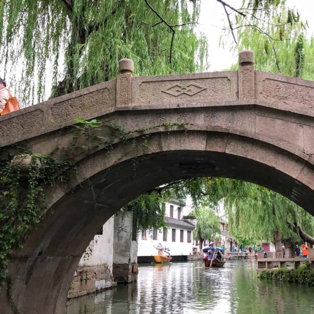 An ancient carved stone bridge crossing the canal with a weeping willow next to it.