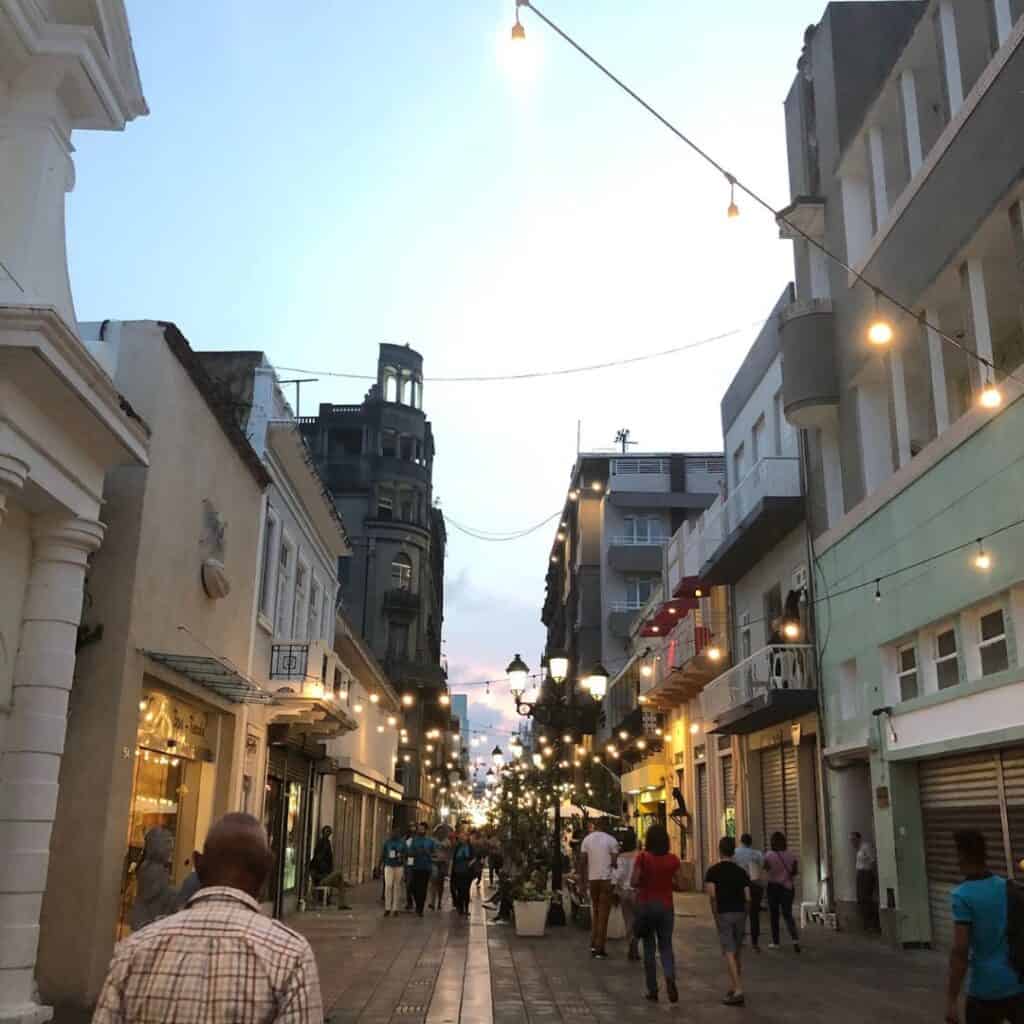 Walking down a pedestrian street in Santo Domingo with lights strung across the street and many people walking by.