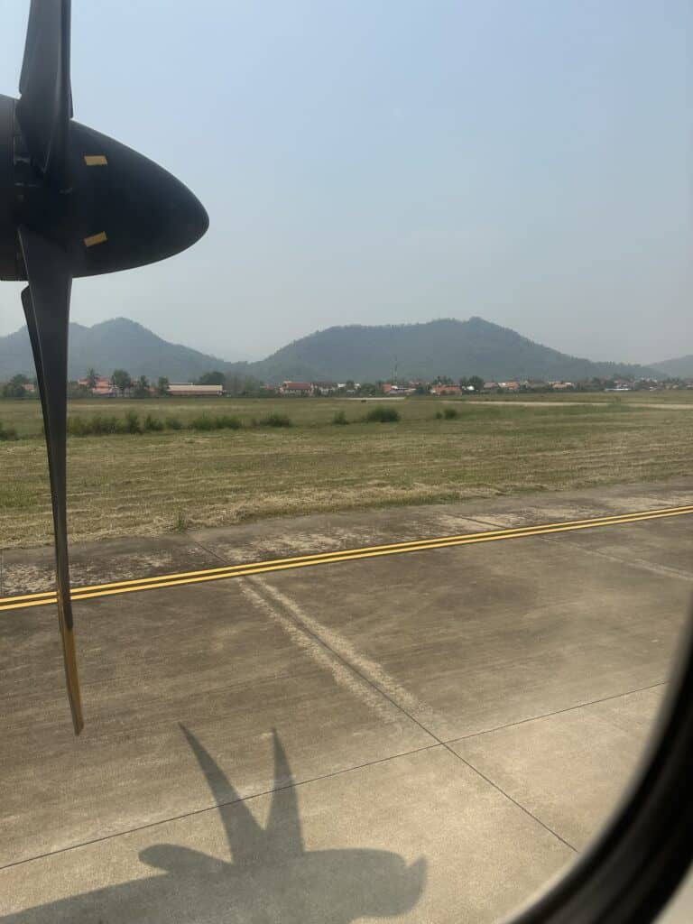 The propeller of the airplane leaving the Luang Prabang airport with low mountains in the background