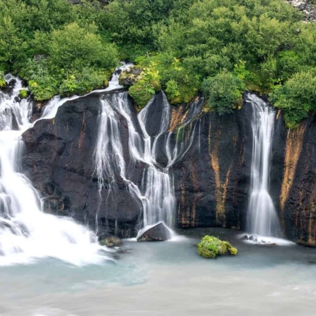 A waterfall tumbling down a brown rock cliff face with green trees along the top.