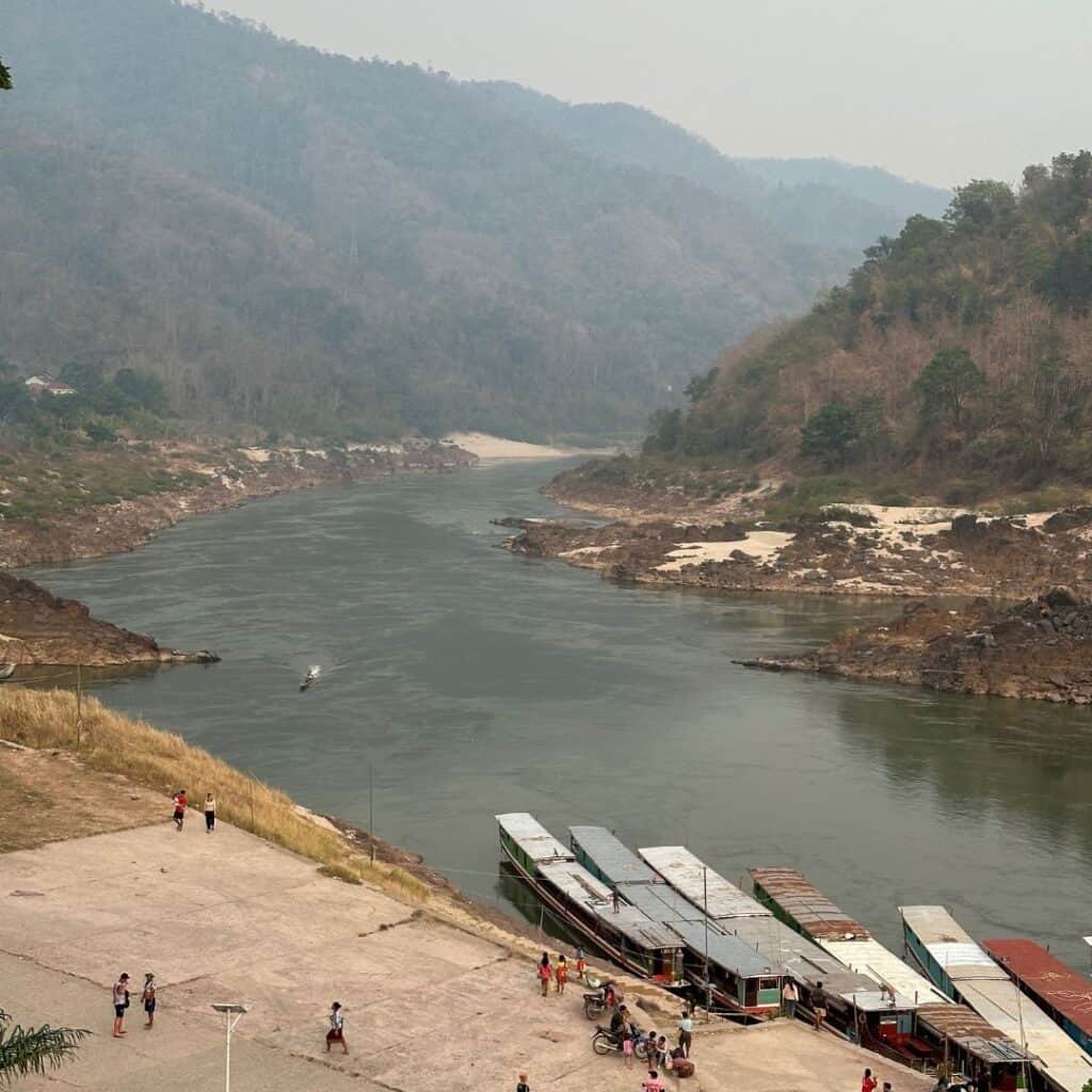 The slow boat dock in Pakbang with the river and the landing area with a few people standing there.