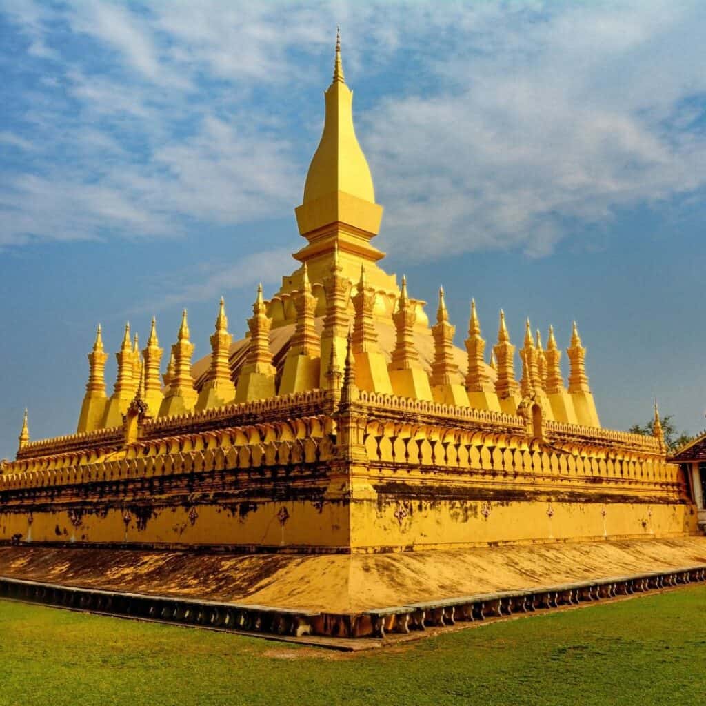 A bright shiny gold temple in Laos with a high rounded pointed tower in the middle.