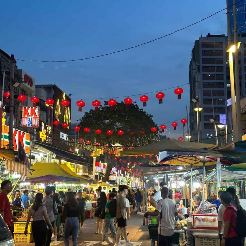 A busy food street in Kuala Lumpur with lights strung across the street.