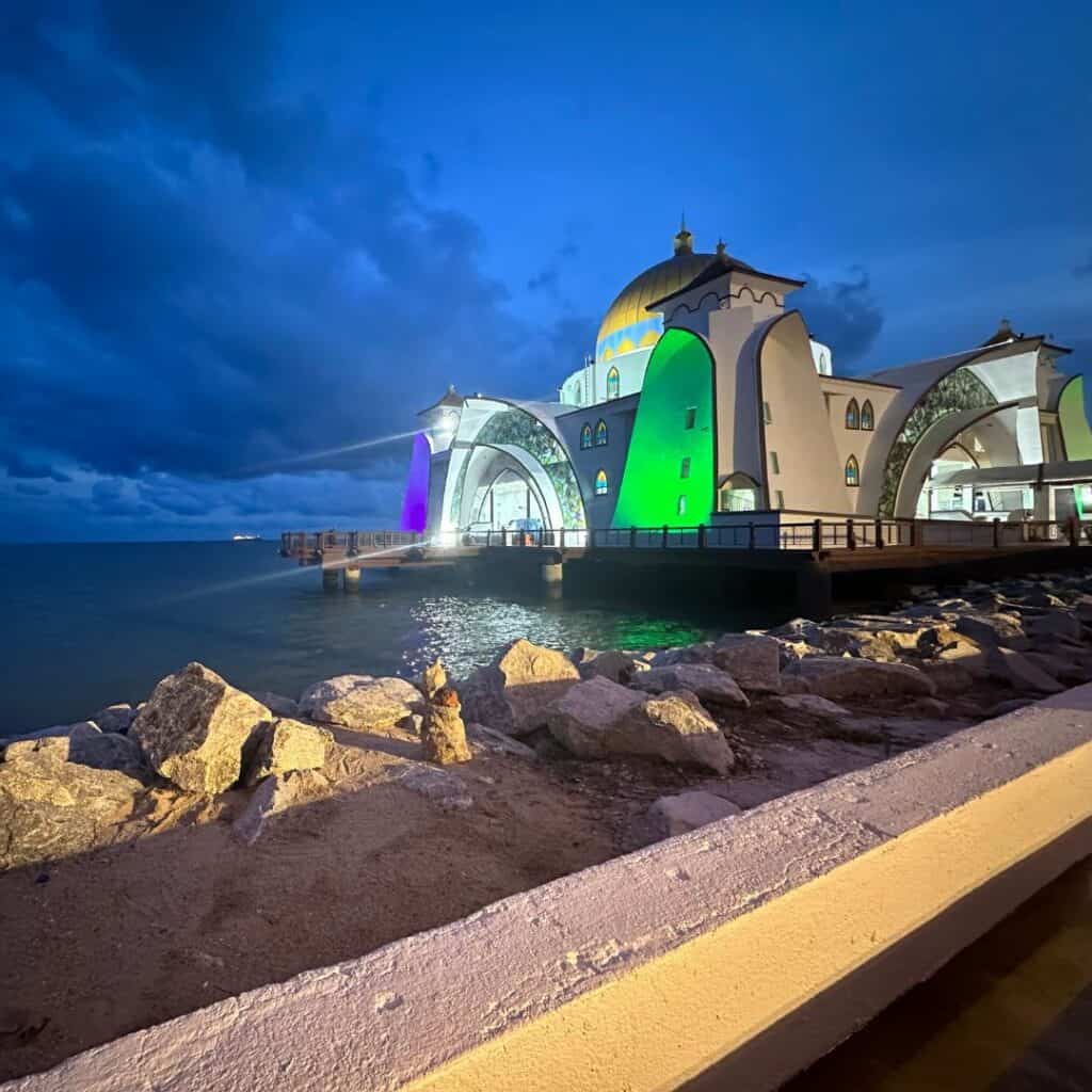 A brightly colored mosque standing on the shore against a deep blue sky.