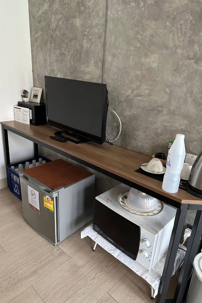 The TV shelf area with the mini fridge, microwave, and dishes.