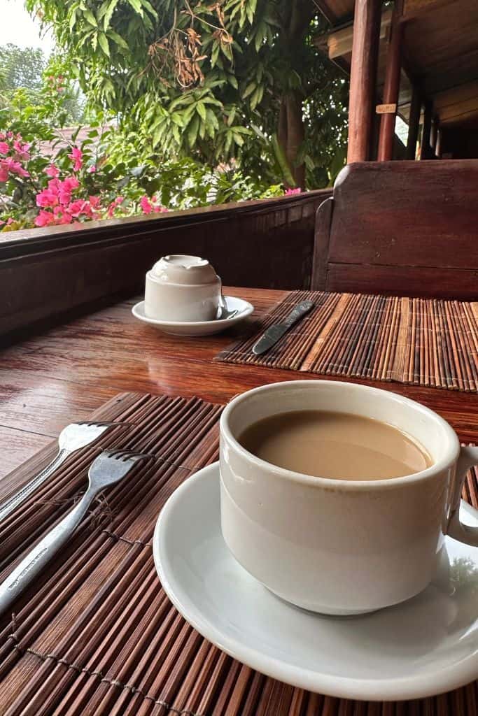 The cup of Laotian coffee on the wooden table in the outdoor dining area of the restaurant across from the Mekong Riverside Lodge