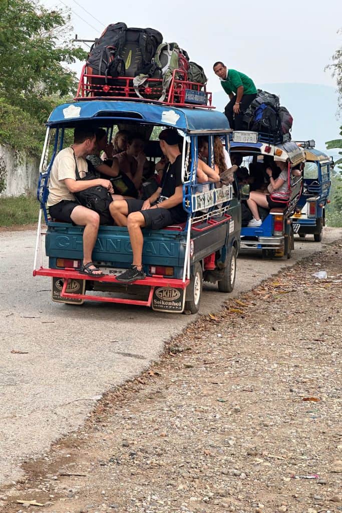 Many people stuffed into an open sided truck with luggage stacked up top.