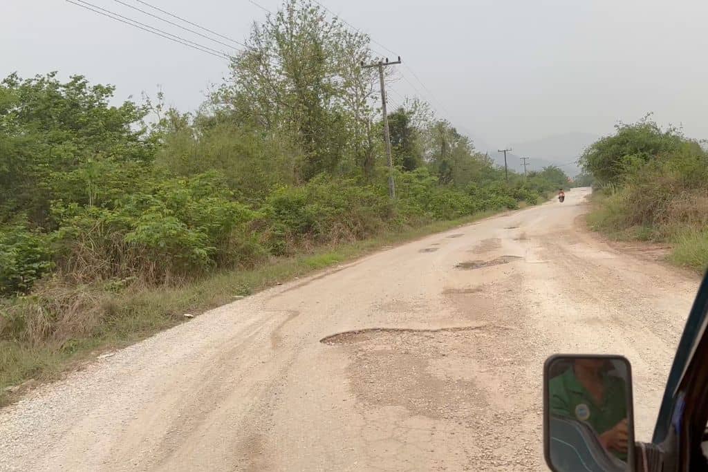 A shot of the dirt road curving to the right and showing several large potholes.