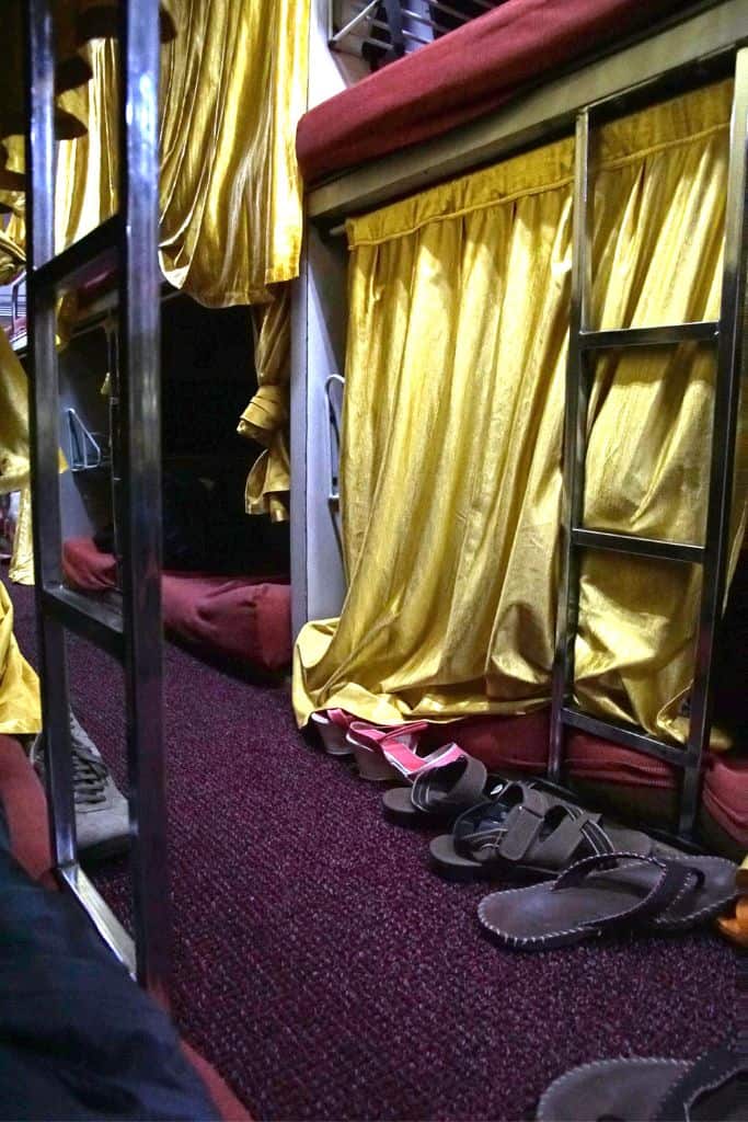 The dark interior of an Asian sleeper bus with red cushions and a gold curtain for privacy.