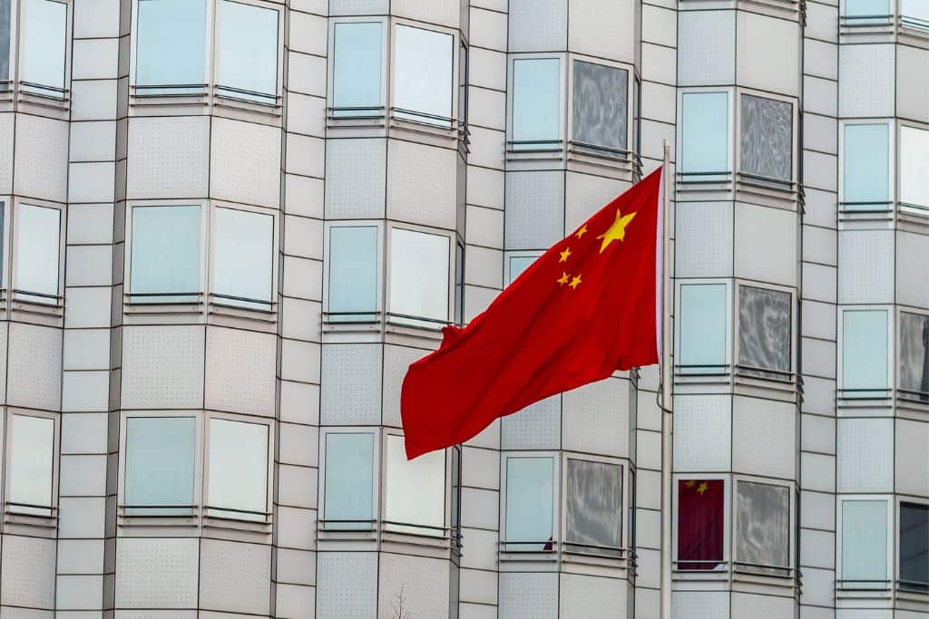 The red Chinese flag flying in front of the large embassy building.