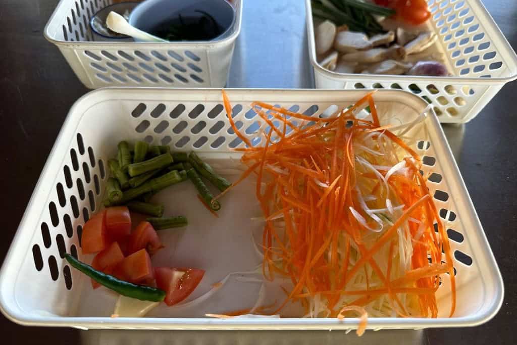 A white rectangular plastic basket holding the prepped ingredients for the papaya salad.