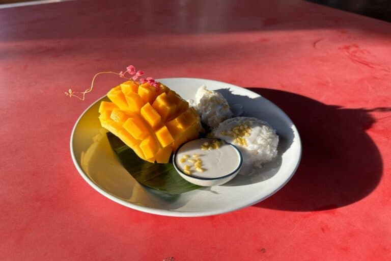 A beautiful presentation of cubed mango sitting in the skin with a white dish of coconut cream sauce to dip it in.