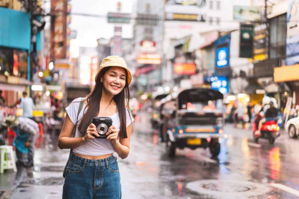 A young female tourist in China standing on a busy street with her camera around her neck.