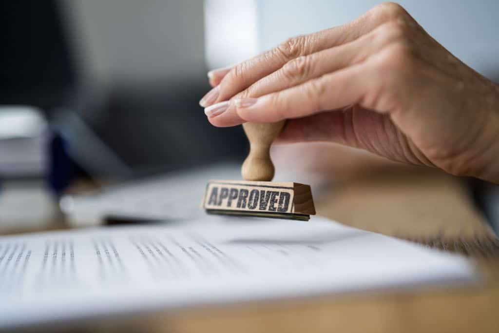 A hand holding the approved stamp over a piece of paper.