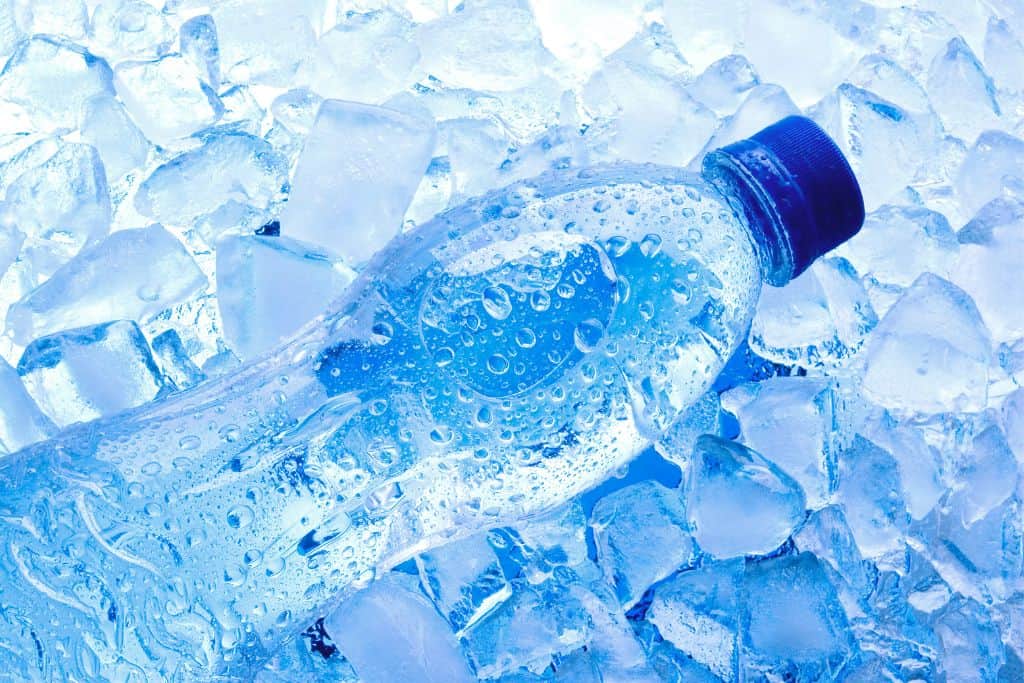 An ice cold bottle of water laying on a bed of ice cubes.