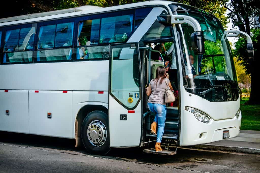 A large white bus with a young woman getting on board.