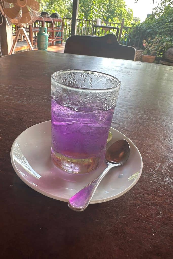 A half glass of pea blossom lemonade which glows a lovely light purple color in a chilled glass.