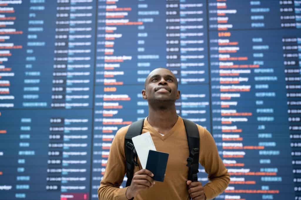 A young man standing in front of an arrivals and departures board at the airport.