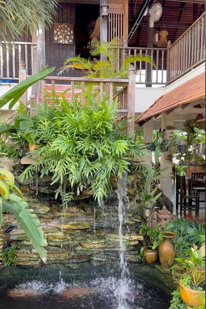 The lush green garden around a koi pond with the wooden stairs going to the second floor level cooking area.