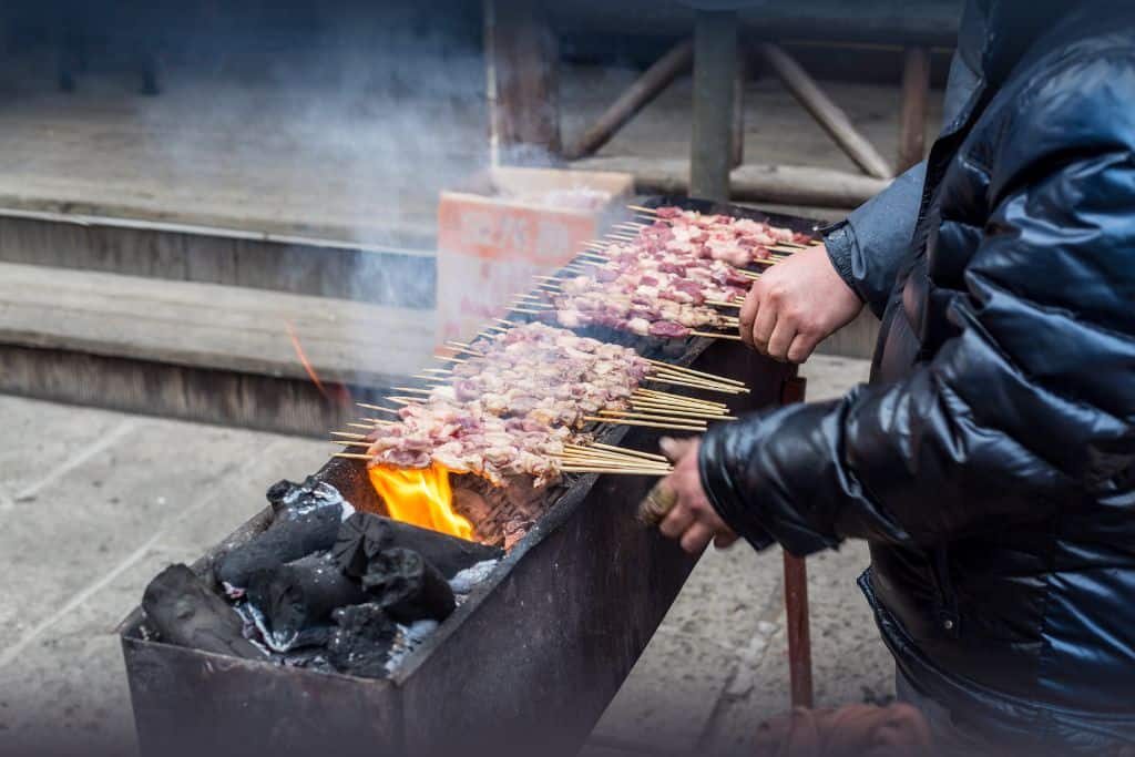 Lamb skewers being grilled on the street on a low barbecue grill.