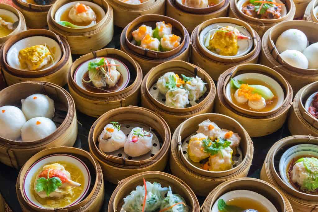 Large assortment of dim sum, small sized foods in bamboo steamer baskets.